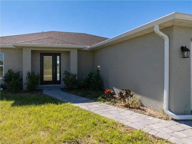 Entrance to property with a yard, stucco siding, and roof with shingles
