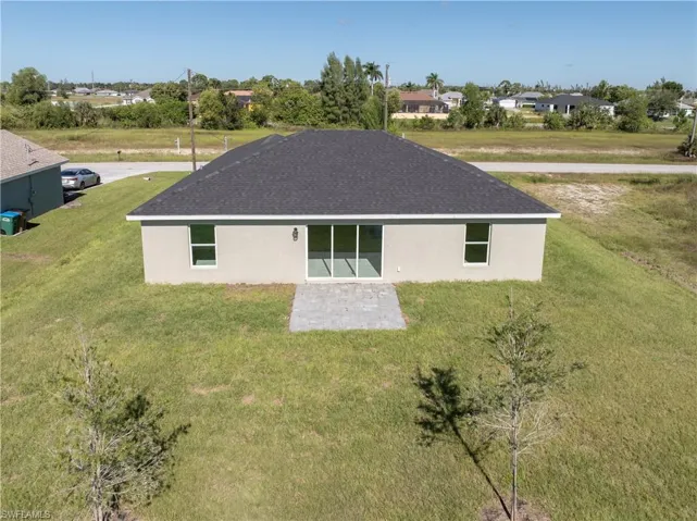 Back of house featuring a yard, stucco siding, a residential view, and roof with shingles