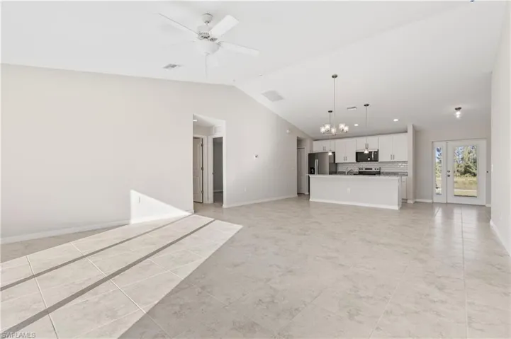 Unfurnished living room with a chandelier, vaulted ceiling, a ceiling fan, and light tile patterned flooring