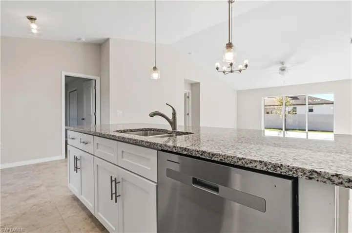 Kitchen with stainless steel dishwasher, white cabinets, light stone counters, hanging light fixtures, and ceiling fan