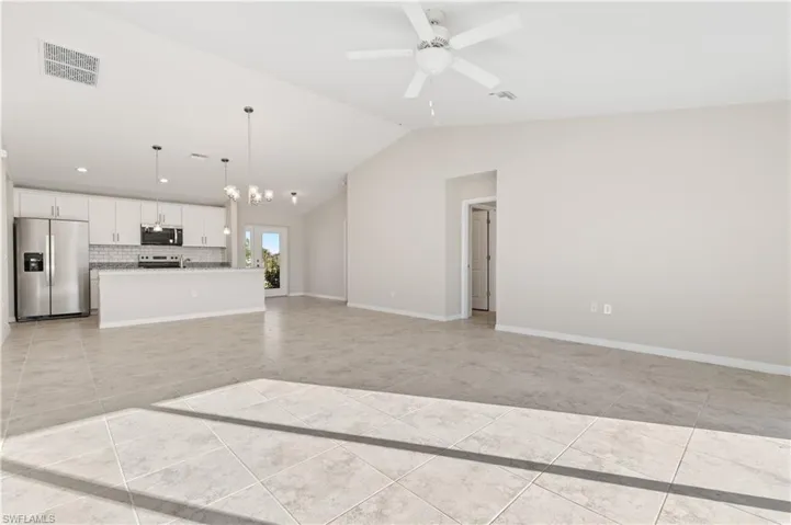 Unfurnished living room with vaulted ceiling, light tile patterned flooring, a chandelier, and ceiling fan