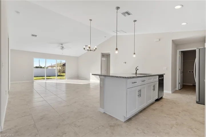 Kitchen featuring decorative light fixtures, a chandelier, dark stone countertops, vaulted ceiling, and appliances with stainless steel finishes