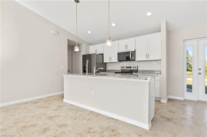 Kitchen with light stone countertops, white cabinetry, appliances with stainless steel finishes, tasteful backsplash, and decorative light fixtures