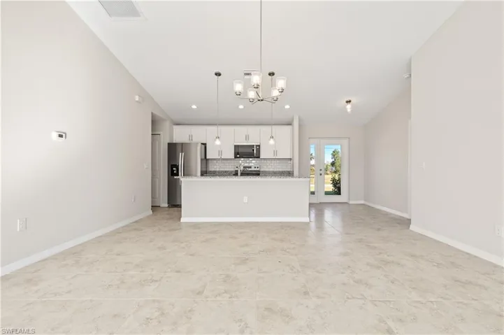 Kitchen featuring decorative backsplash, a kitchen island with sink, open floor plan, pendant lighting, and white cabinets