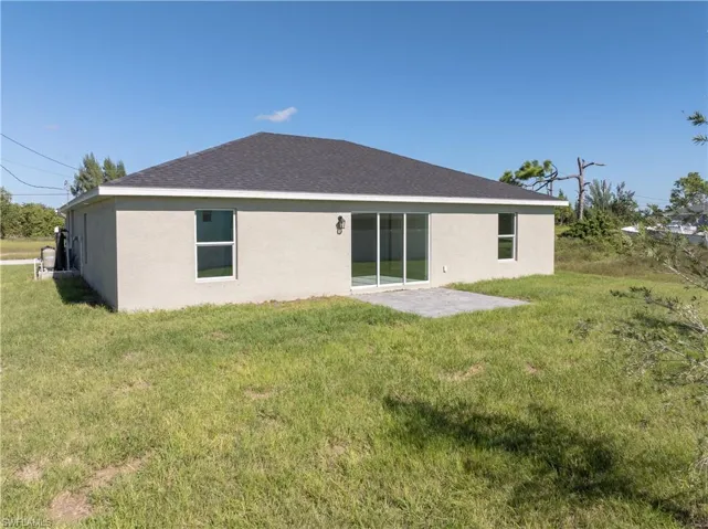 Back of house featuring a patio, stucco siding, a yard, and roof with shingles