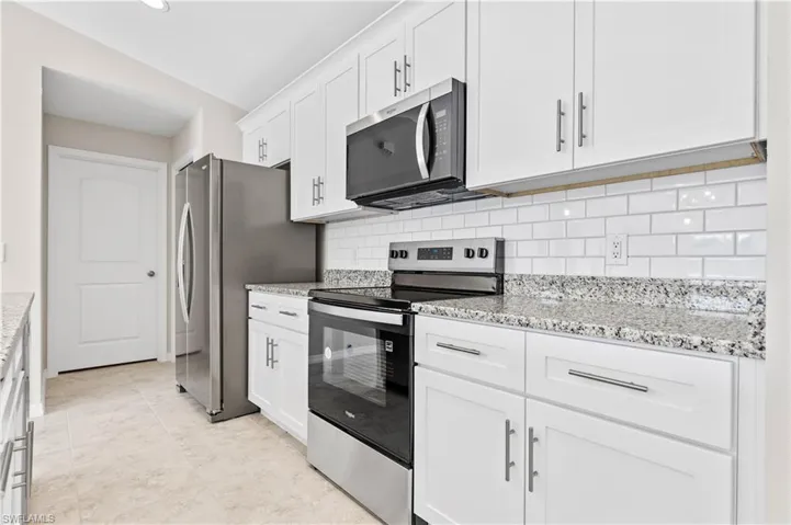Kitchen featuring stainless steel appliances, white cabinetry, light stone countertops, tasteful backsplash, and lofted ceiling