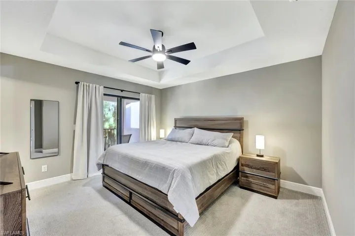Bedroom featuring a tray ceiling, ceiling fan, light carpet, and access to outside