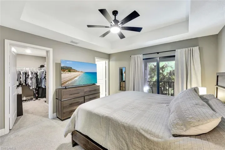 Bedroom featuring light carpet, a walk in closet, a raised ceiling, ceiling fan, and a closet