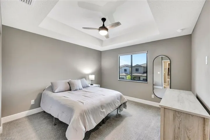 Carpeted bedroom with a raised ceiling and ceiling fan