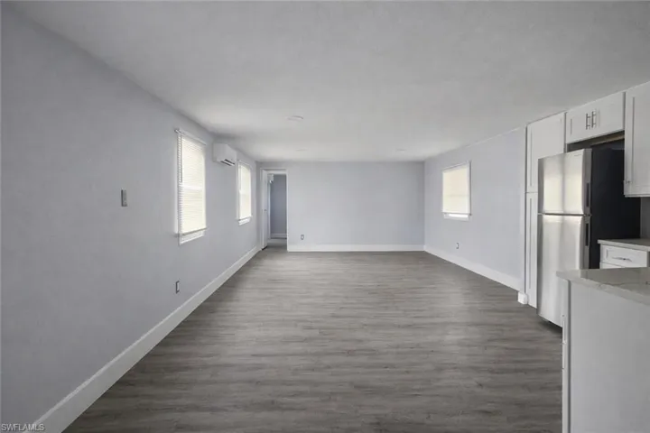 Unfurnished living room featuring dark wood-style floors and baseboards