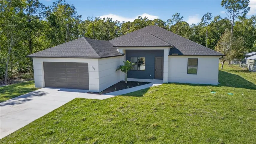View of front of property with a shingled roof, a front yard, an attached garage, concrete driveway, and view of scattered trees
