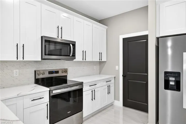 Kitchen featuring stainless steel appliances, backsplash, white cabinets, and light stone countertops