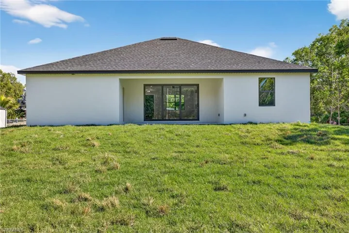 Rear view of property featuring roof with shingles, stucco siding, a lawn, and a patio area