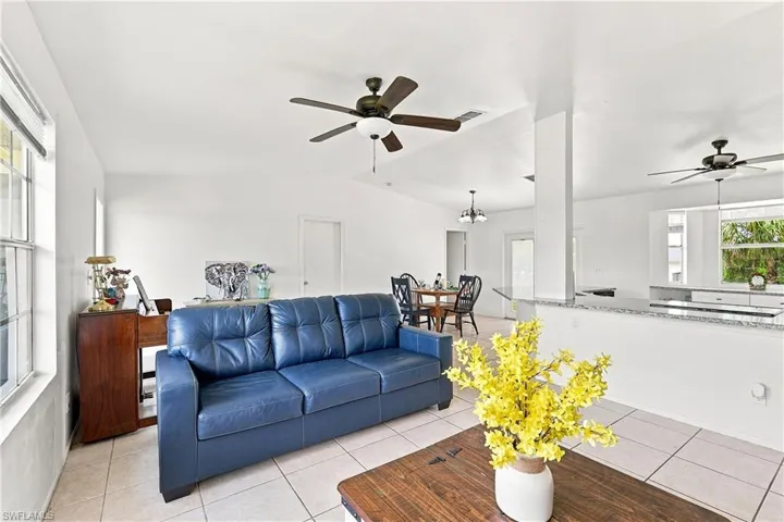 Open-concept living area featuring light-toned tile flooring, white walls, and a ceiling fan with integrated lighting