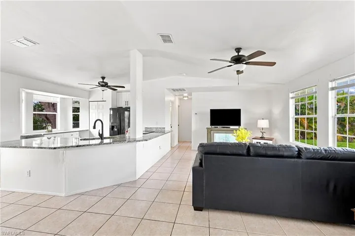 Spacious interior featuring a kitchen island with granite-finish countertops, black appliances, white cabinetry, and tile flooring