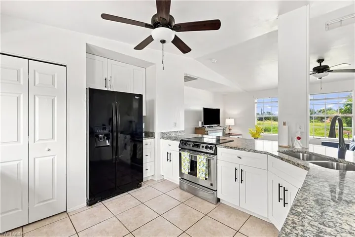 Kitchen featuring white cabinetry, granite countertops, stainless steel electric range, a black side-by-side refrigerator, and tile flooring