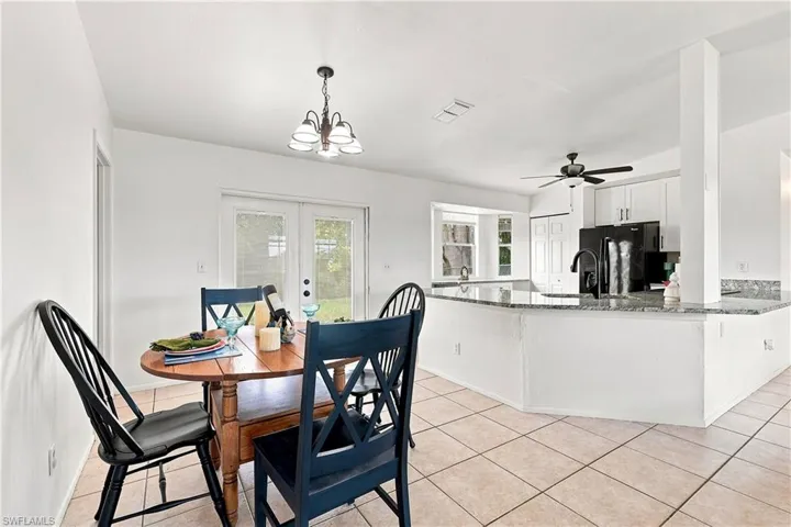 Open-concept dining and kitchen area featuring tile flooring, a breakfast bar with stone countertops, white cabinetry, a bay window, and French patio doors