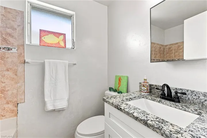 Bathroom with a granite-style countertop vanity, white under-mount sink, and matte black faucet