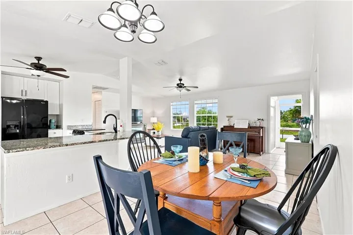 Open-concept dining area featuring a contemporary chandelier, tile flooring, and integrated access to the kitchen's breakfast bar with granite-style countertops and a black gooseneck faucet