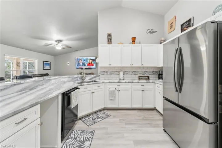 Kitchen featuring freestanding refrigerator, dishwasher, vaulted ceiling, a sink, and a ceiling fan
