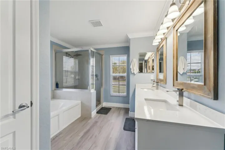 Bathroom featuring crown molding, a shower stall, a bath, double vanity, and wood finished floors