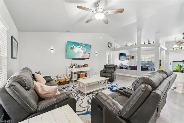 Living room with lofted ceiling, a ceiling fan, and light wood-style floors