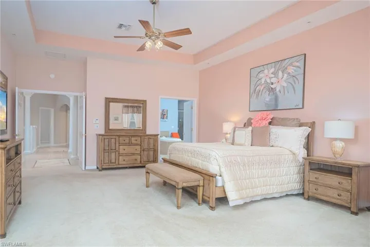 Bedroom with light carpet, ensuite bathroom, a raised ceiling, and ceiling fan