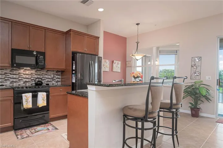 Kitchen featuring hanging light fixtures, tasteful backsplash, dark stone countertops, a kitchen island, and black appliances