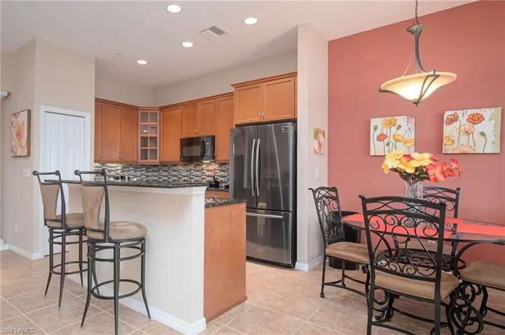 Kitchen featuring stainless steel fridge, tasteful backsplash, a breakfast bar, pendant lighting, and light tile patterned flooring