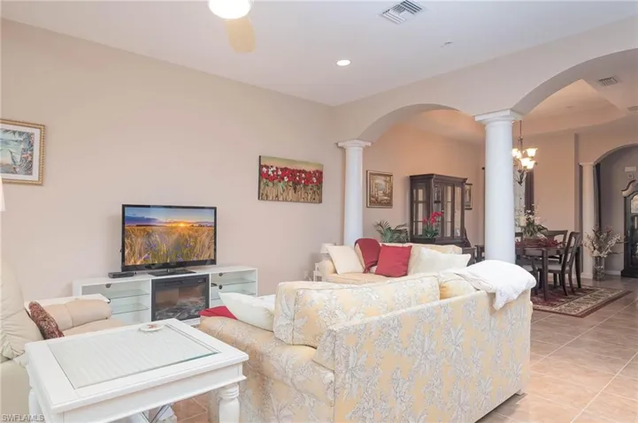 Tiled living room featuring ceiling fan with notable chandelier and ornate columns