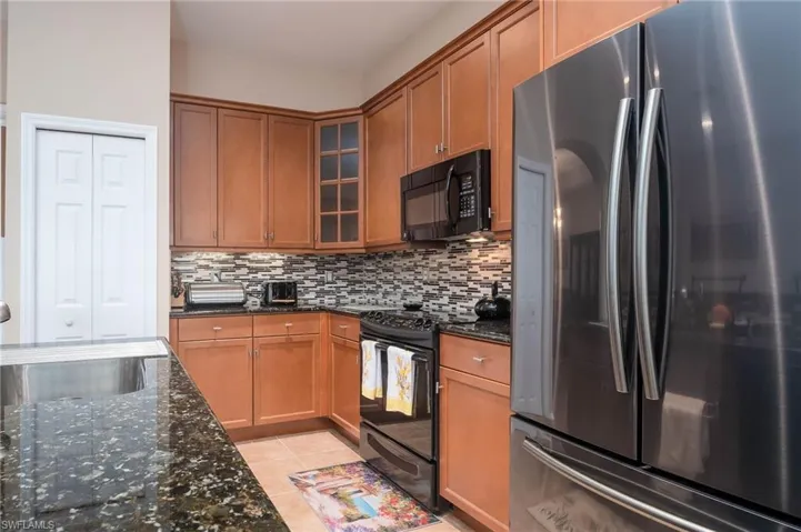 Kitchen with backsplash, dark stone counters, black appliances, sink, and light tile patterned floors