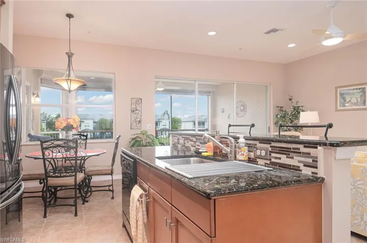 Kitchen featuring decorative backsplash, decorative light fixtures, a center island with sink, and dark stone countertops