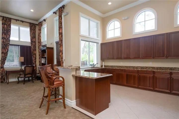 Kitchen with a high ceiling, crown molding, stone countertops, a breakfast bar area, and light tile patterned flooring