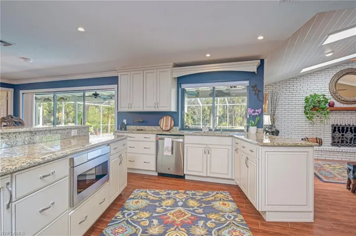 Kitchen with light stone countertops, white cabinetry, stainless steel appliances, light wood finished floors, and brick wall