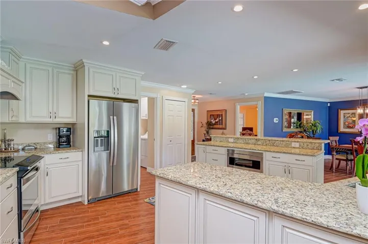Kitchen with stainless steel appliances, crown molding, light stone countertops, tiled floors, and custom cabinetry