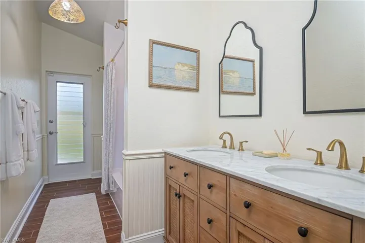 Full Pool bath with wainscoting, double vanity, shower / tub combo, tiled floors, and lofted ceiling