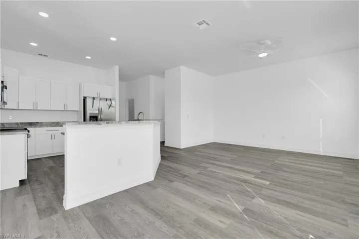 Kitchen featuring a center island with sink, white cabinets, ceiling fan, stainless steel fridge with ice dispenser, and light wood-type flooring