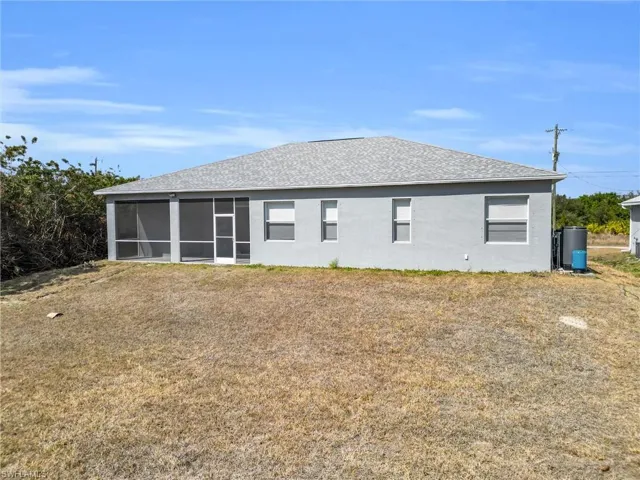 Back of house with a lawn, stucco siding, a shingled roof, and a sunroom