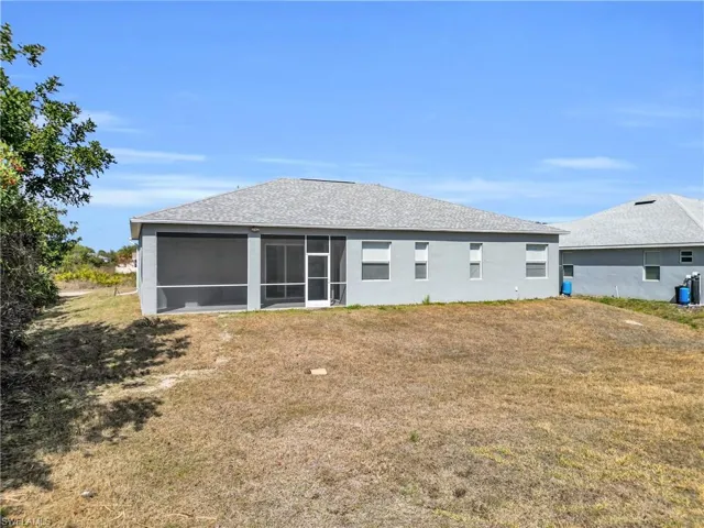 Back of property with a lawn, a sunroom, stucco siding, and roof with shingles