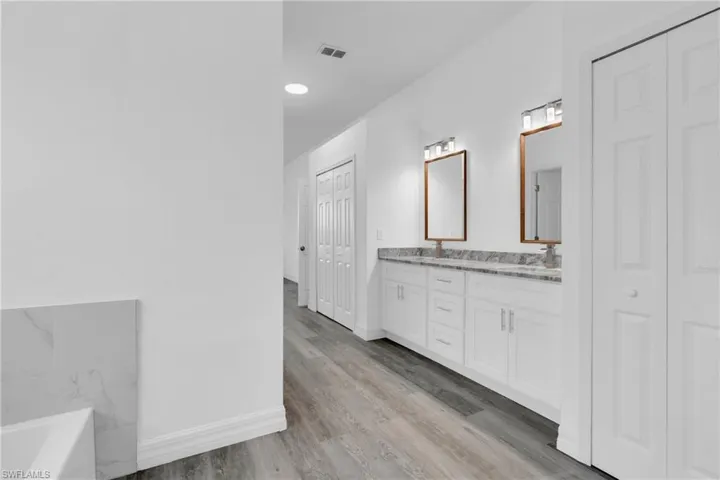 Full bathroom featuring a closet, double vanity, a bathtub, and light wood-style flooring