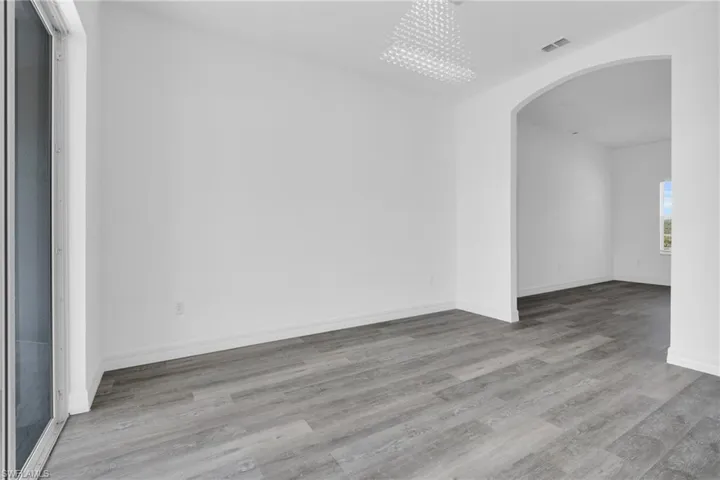 Empty room with arched walkways, light wood-style flooring, and a chandelier