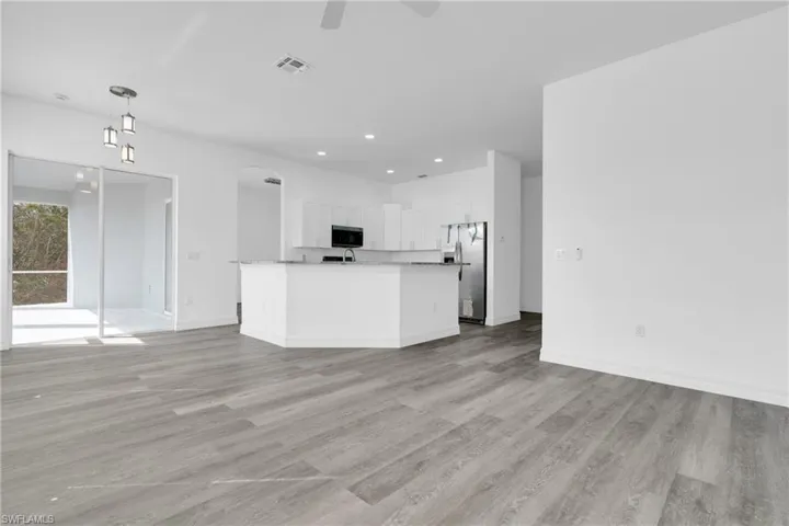 Kitchen with stainless steel fridge, open floor plan, white cabinets, and a center island with sink