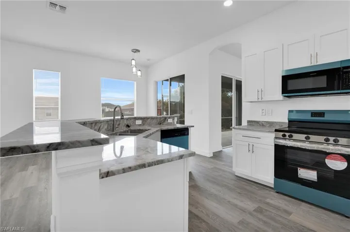 Kitchen featuring stainless steel appliances, white cabinets, and light stone countertops