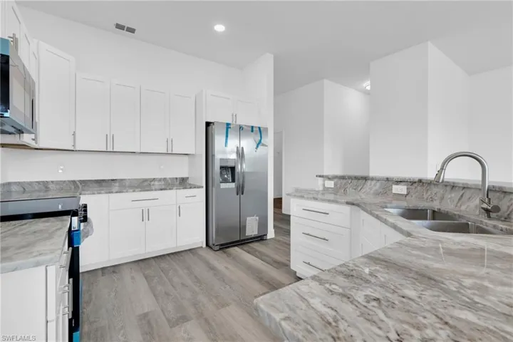 Kitchen featuring stainless steel appliances, light stone counters, light wood finished floors, white cabinets, and recessed lighting