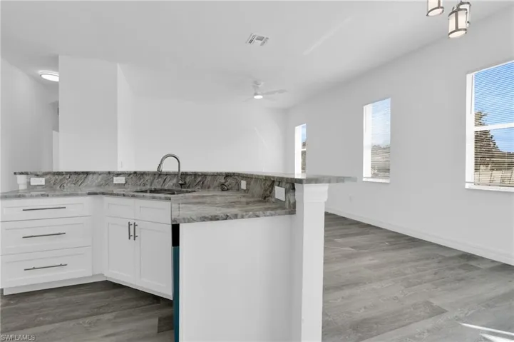 Kitchen with white cabinetry, light wood-style floors, a ceiling fan, and light stone counters
