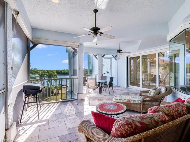Sunroom with stone tile flooring, outdoor dining space, ceiling fan, a textured ceiling, and a water view