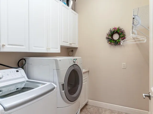 Laundry room with light tile patterned flooring, washing machine and clothes dryer, and cabinet space