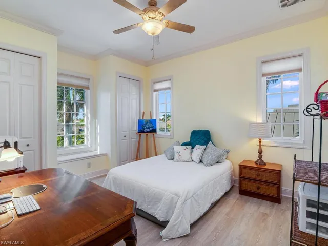 Bedroom featuring multiple closets, multiple windows, wood finished floors, crown molding, and a ceiling fan
