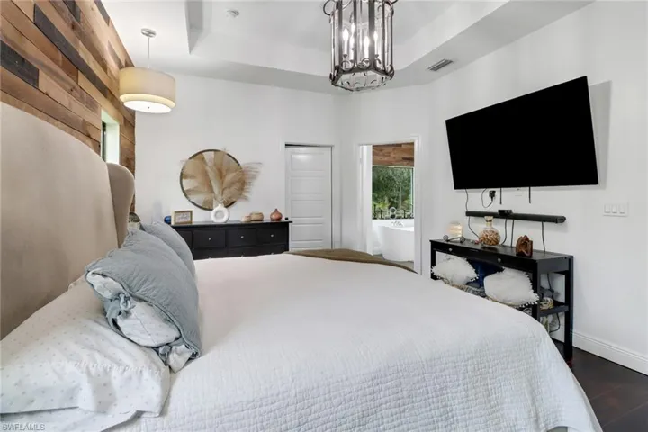 Bedroom featuring dark wood-type flooring, a notable chandelier, and a tray ceiling
