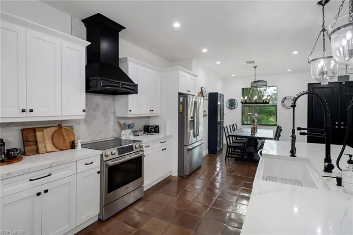 Kitchen with decorative light fixtures, white cabinetry, custom exhaust hood, stainless steel appliances, and decorative backsplash